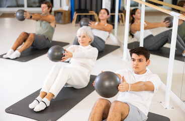 Slim young man practicing pilates with ball in training area during pilates classes