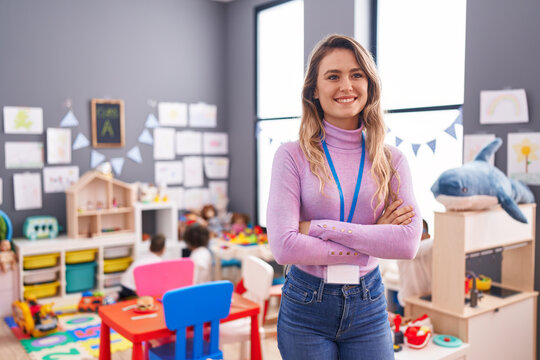 Young blonde woman teacher smiling confident standing with arms crossed gesture at kindergarten