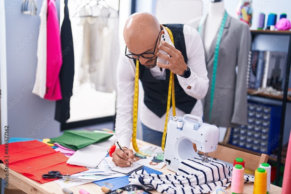 Sticker Young bald man tailor talking on smartphone writing on notebook at tailor shop