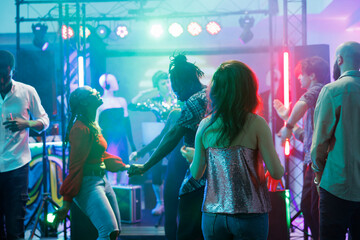 Party dancers making moves on dancefloor while having fun and relaxing in nightclub. People attending discotheque and dancing while enjoying music in club illuminated with stage lights