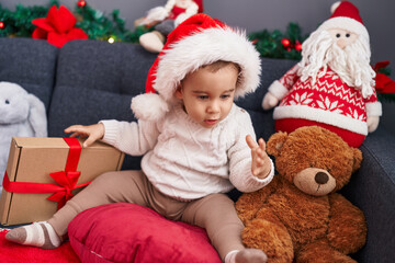 Fototapeta na wymiar Adorable hispanic toddler wearing christmas hat sitting on sofa at home