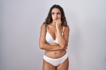 Naklejka premium Young hispanic woman wearing white lingerie looking stressed and nervous with hands on mouth biting nails. anxiety problem.