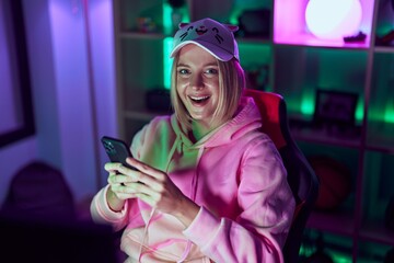 Young blonde woman streamer using smartphone at gaming room