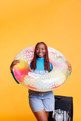Joyful woman travelling on vacation with inflatable ring and suitcase, feeling cheerful about holiday trip. Smiling tourist enjoying international getaway abroad, carrying trolley bags.