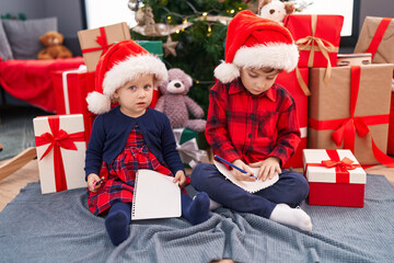 Adorable boy and girl drawing on notebook celebrating christmas at home