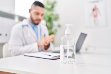 Young latin man doctor using laptop using sanitizer gel hands at clinic