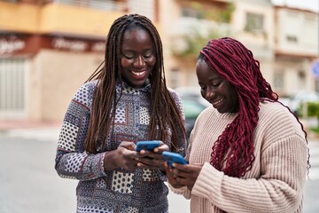 African american women friends smiling confident using smartphone at street
