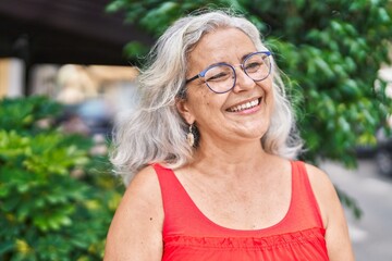 Middle age grey-haired woman smiling confident looking to the side at park