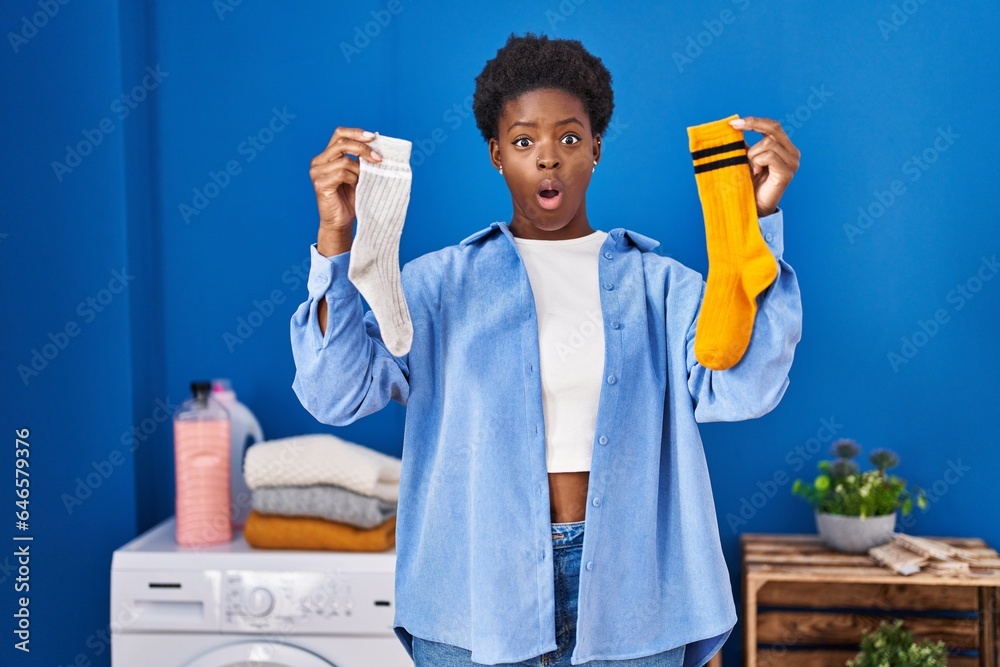 Sticker African american woman holding clean andy dirty socks afraid and shocked with surprise and amazed expression, fear and excited face.