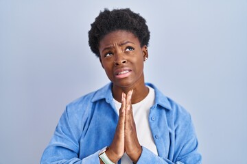 African american woman standing over blue background begging and praying with hands together with...