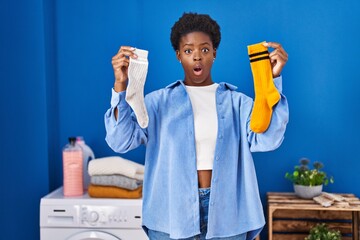African american woman holding clean andy dirty socks afraid and shocked with surprise and amazed...