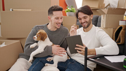 Two men couple using touchpad sitting on floor with dog at new home