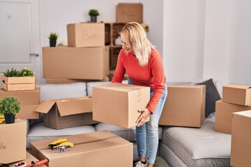 Young blonde woman smiling confident holding package at new home