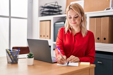 Young blonde woman business worker using laptop writing on notebook at office