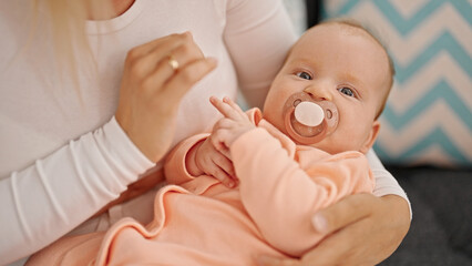 Mother and daughter sitting on sofa sucking pacifier at home