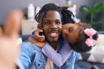 Father and daughter making selfie by camera sitting on sofa at home