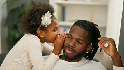 Obraz premium African american father and daughter sitting on sofa telling secret at home