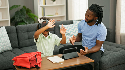 African american father and daughter sitting on sofa studying and playing using virtual reality glasses at home