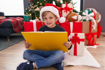 Obraz na płótnie Canvas Adorable toddler reading book sitting by christmas tree at home