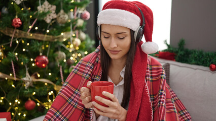 Young beautiful hispanic woman listening to music drinking coffee celebrating christmas at home