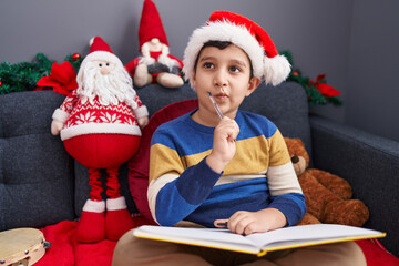 Adorable hispanic boy writing on notebook sitting on sofa by christmas decoration at home