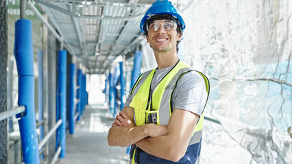 Young hispanic man architect smiling confident standing with arms crossed gesture at construction place