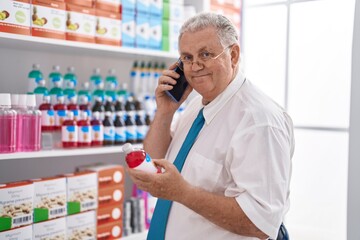 Middle age grey-haired man customer talking on smartphone holding medication bottle at pharmacy