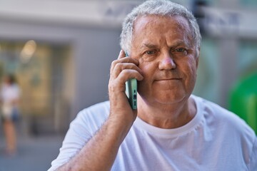 Middle age grey-haired man talking on smartphone with relaxed expression at street
