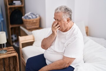 Middle age grey-haired man sitting on bed yawning at bedroom