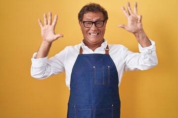 Middle age hispanic man wearing professional cook apron showing and pointing up with fingers number nine while smiling confident and happy.