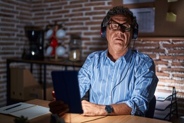 Obraz premium Middle age hispanic man using touchpad sitting on the table at night relaxed with serious expression on face. simple and natural looking at the camera.