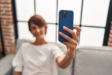 Young beautiful hispanic woman make selfie by smartphone sitting on sofa at home