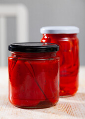 Glass jar of homemade marinated red bell peppers on wooden background
