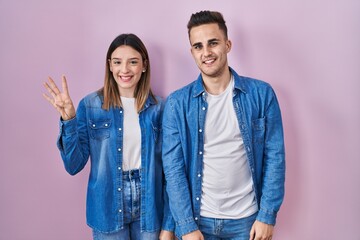 Young hispanic couple standing over pink background showing and pointing up with fingers number four while smiling confident and happy.
