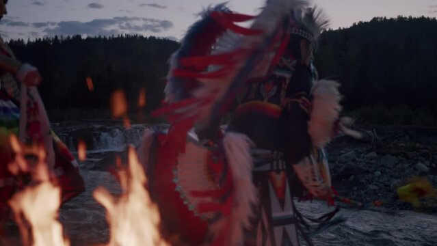 Native American Indigenous Dancing by the fireplace at sunset in Alberta Canada wearing traditional Tsu'Tina Fancy Dance Regalia. Cinematic Footage of Indigenous Fancy Dance at Sunset in Slow motion.