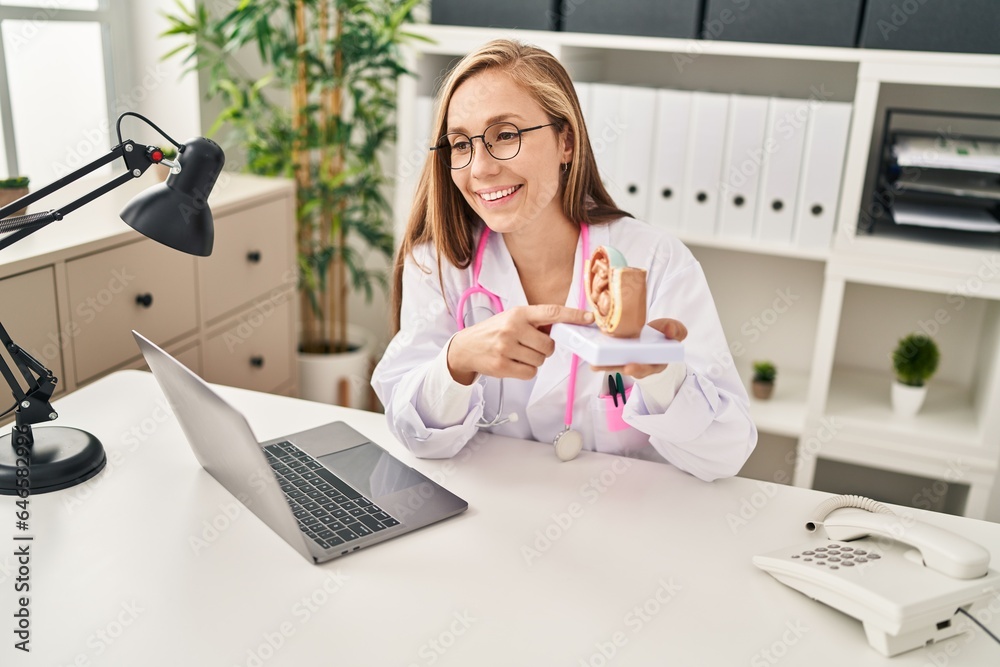 Wall mural Young blonde woman gynecologist holding anatomical model of uterus at clinic