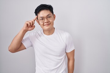 Young asian man standing over white background smiling pointing to head with one finger, great idea or thought, good memory