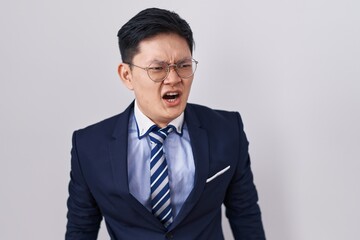 Young asian man wearing business suit and tie angry and mad screaming frustrated and furious, shouting with anger. rage and aggressive concept.
