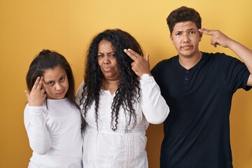 Family of mother, daughter and son standing over yellow background shooting and killing oneself pointing hand and fingers to head like gun, suicide gesture.