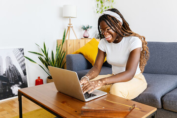 Happy young student woman with vitiligo studying on laptop sitting on sofa at home. Education and...