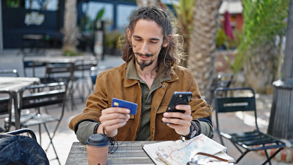 Young hispanic man tourist using smartphone sitting on table at coffee shop terrace