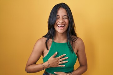 Obraz premium Brunette woman standing over yellow background smiling and laughing hard out loud because funny crazy joke with hands on body.
