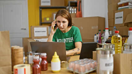 Young woman volunteer using laptop and touchpad talking on smartphone at charity center