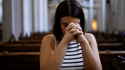 Young beautiful hispanic woman praying on a church bench at Augustinian Church in Vienna