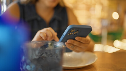 Young beautiful hispanic woman using smartphone sitting on the table at the restaurant