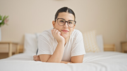 Young beautiful hispanic woman lying on bed smiling at bedroom
