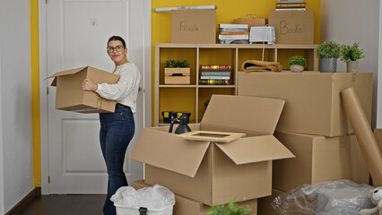 Fototapeta premium Young beautiful hispanic woman walking in holding package at new home