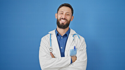 Young hispanic man doctor smiling confident standing with arms crossed gesture over isolated blue background