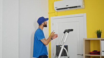Young hispanic man technician repairing air condition machine using remote control at home