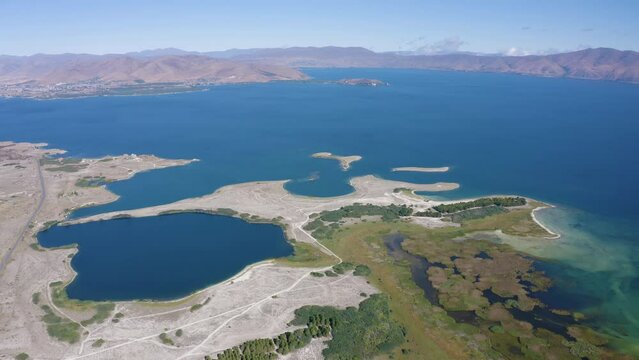 Backward reveal aerial shot of Sevan Lake and Norashen Reserve on sunny summer day. Gegharkunik Province, Armenia.